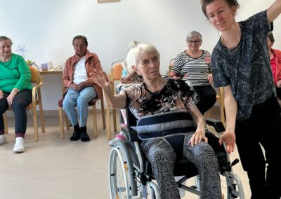 Usměvavá seniorka na vozíku a lektorka při tanci
