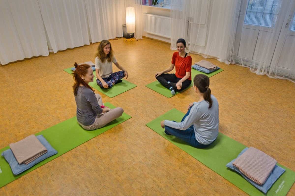 Sál s karimatkami, polštáři a dekami a skupina žen sedících v kruhu